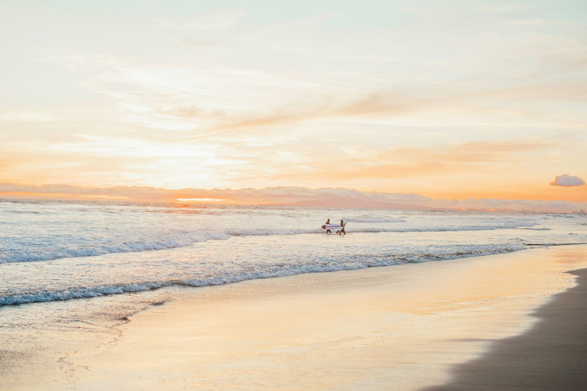 A peaceful beach scene at sunset, with gentle waves and a warm sky. Two people walk along the shore, enjoying the serene atmosphere.