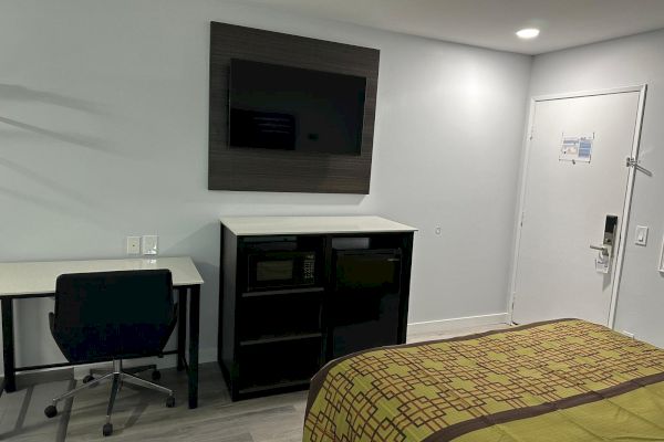 A hotel room with a desk, chair, TV, cabinet, and a bed is visible. The room also has a door on the right side.