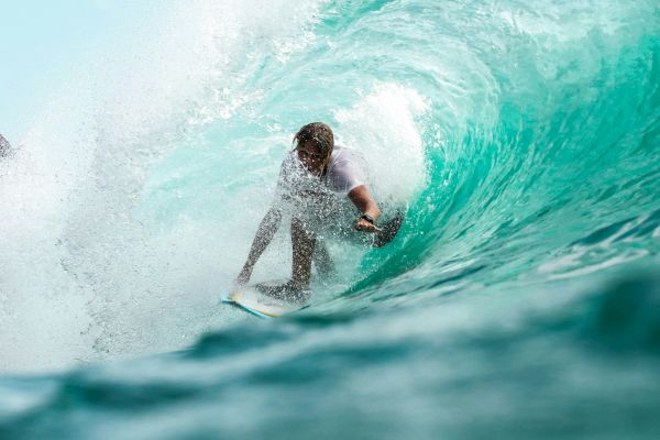 A surfer rides inside a turquoise wave, skillfully maneuvering through the tunnel of water.