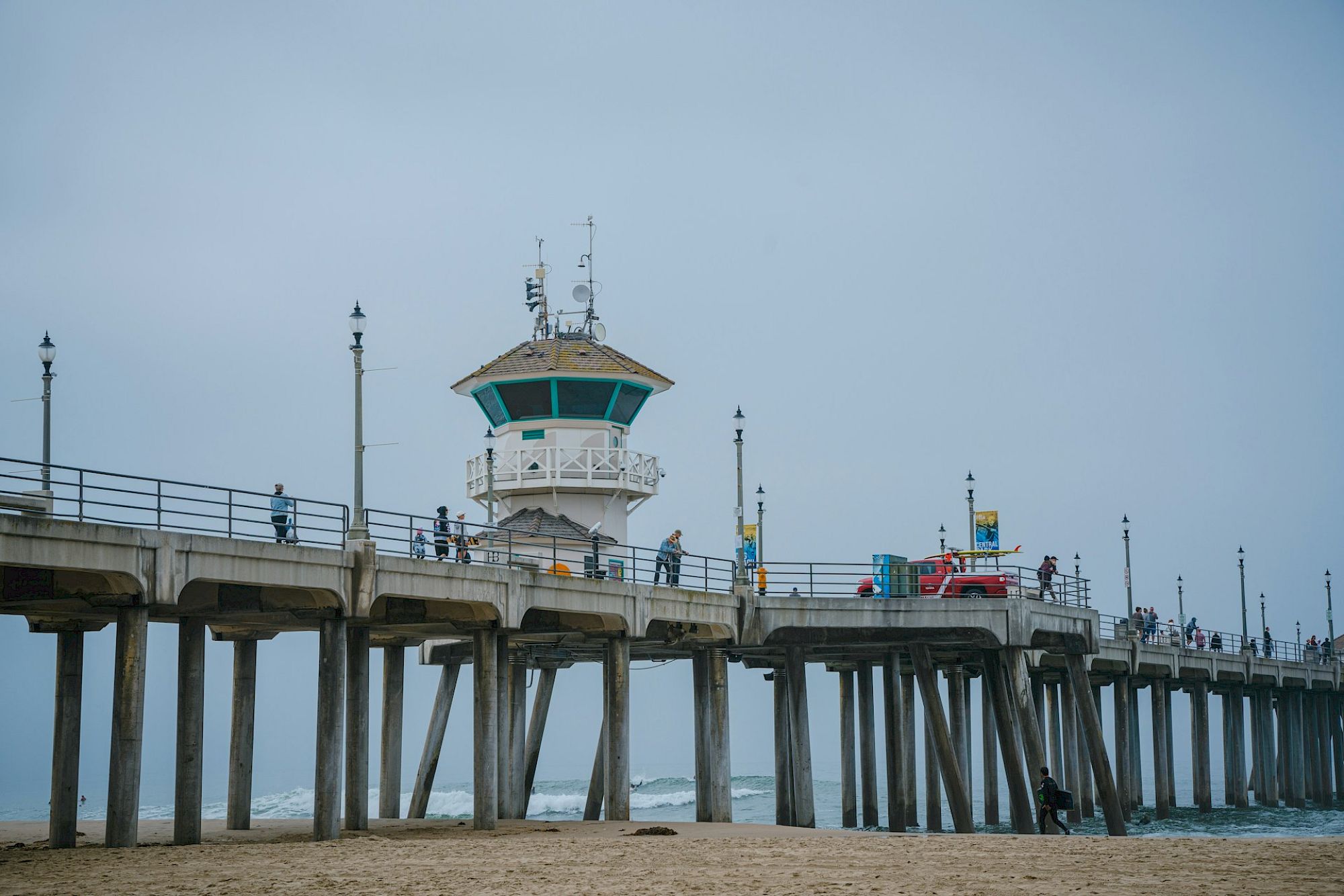 A cloudy scene showing a pier with people walking along it and a structure at the end, next to the ocean with waves.