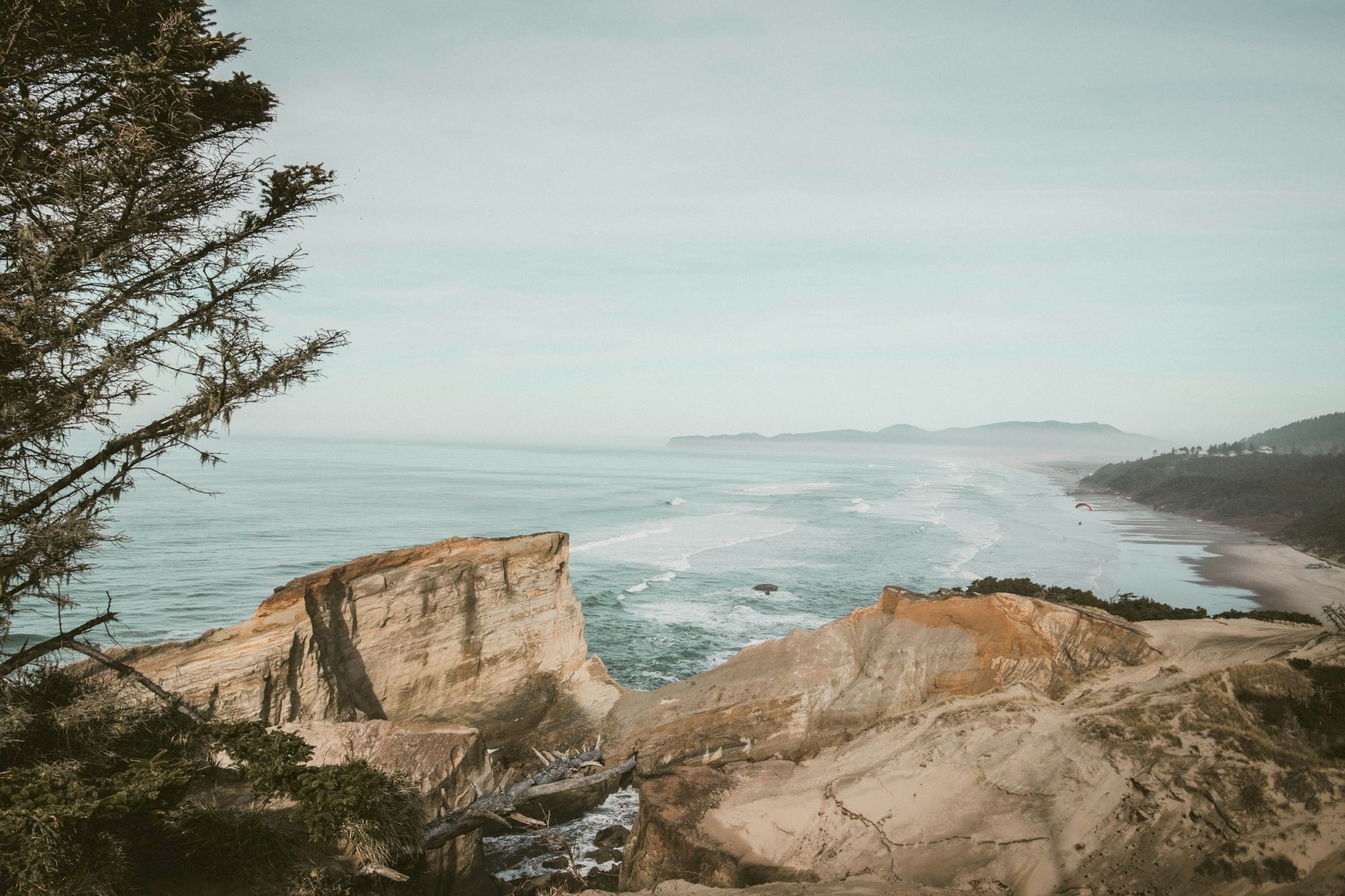 A scenic coastal landscape with cliffs, ocean waves, and distant mountains under a clear sky.