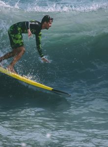 A person is surfing on a wave, balancing on a yellow surfboard, wearing a wetsuit.