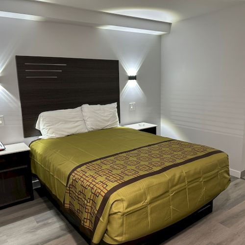 A neatly made bed with green bedding in a modern room, featuring wall-mounted lights and a small nightstand with a phone.