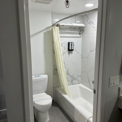 A small bathroom with a toilet, bathtub, shower curtain, and marble wall tiles.