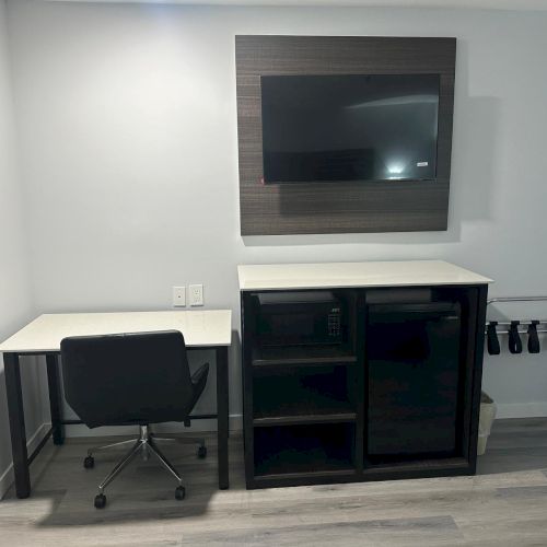 The image shows a room with a desk, chair, wall-mounted TV, cabinet, and luggage rack on the right side of the floor.