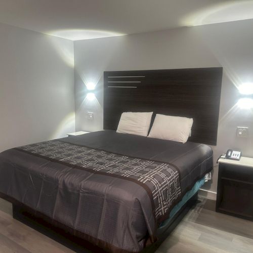 A neatly arranged bedroom features a large bed, two pillows, bedside tables, and modern wall-mounted lights on a wooden headboard.