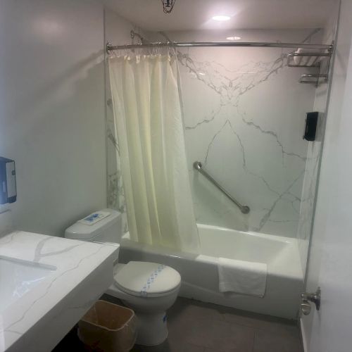 The image shows a bathroom with a sink, toilet, and bathtub. A shower curtain, mirror, and marble-patterned walls are also visible.